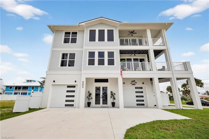 Beach home featuring an attached garage, french doors, concrete driveway, stucco siding, and a balcony - Virtually Edited Image