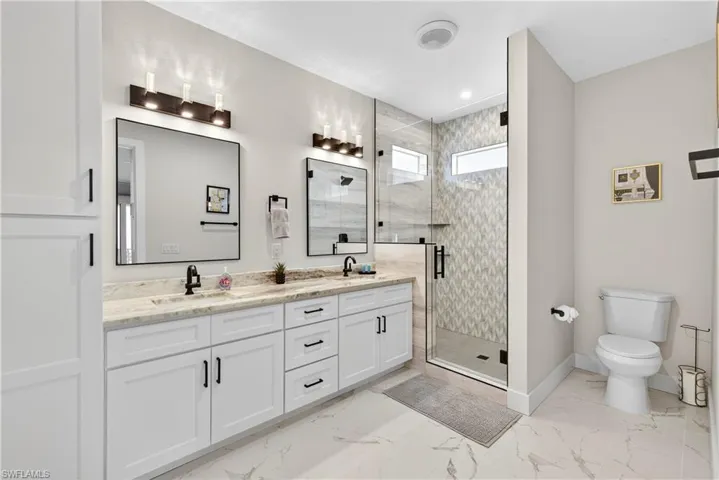 Full bath featuring double vanity, a shower stall, and light marble finish floors - Virtually Edited Image
