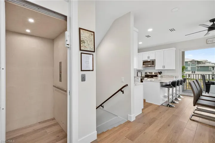 Hallway with an upstairs landing, light wood finished floors, elevator, and recessed lighting - Virtually Edited Image