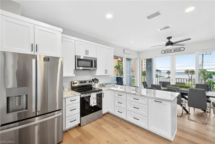 Kitchen with stainless steel appliances, a peninsula, white cabinets, light stone counters, and recessed lighting - Virtually Edited Image