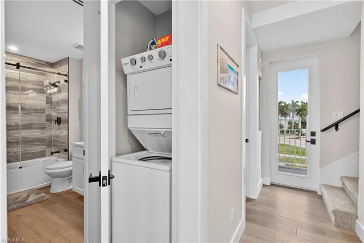 Laundry area featuring light wood-style floors and stacked washing machine and dryer - Virtually Edited Image