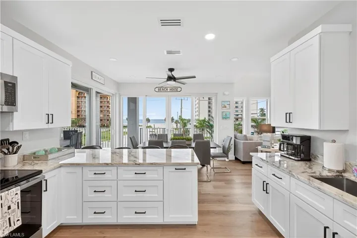 Kitchen featuring a peninsula, open floor plan, light stone countertops, white cabinets, and recessed lighting - Virtually Edited Image