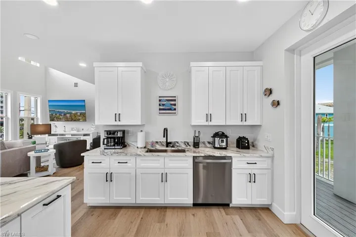 Kitchen featuring white cabinetry, light stone counters, dishwasher, open floor plan, and light wood-type flooring - Virtually Edited Image