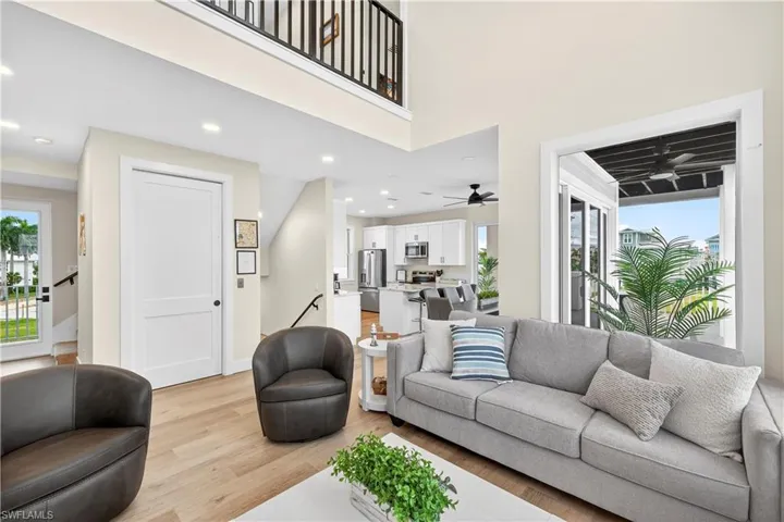 Living room featuring light wood finished floors, healthy amount of natural light, a high ceiling, recessed lighting, and a ceiling fan - Virtually Edited Image