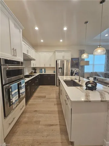 Kitchen featuring white cabinets, appliances with stainless steel finishes, decorative light fixtures, an island with sink, and recessed lighting