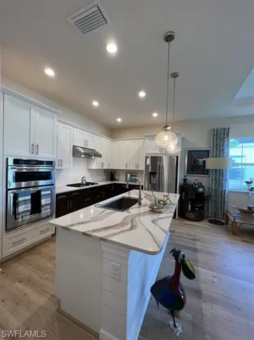 Kitchen with light wood-type flooring, light stone countertops, recessed lighting, a kitchen island with sink, and stainless steel appliances