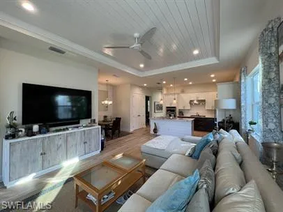 Living area with a ceiling fan, light wood-style flooring, recessed lighting, a raised ceiling, and a chandelier