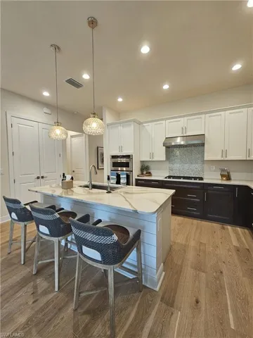 Kitchen featuring white cabinets, hanging light fixtures, light stone counters, a kitchen breakfast bar, and recessed lighting
