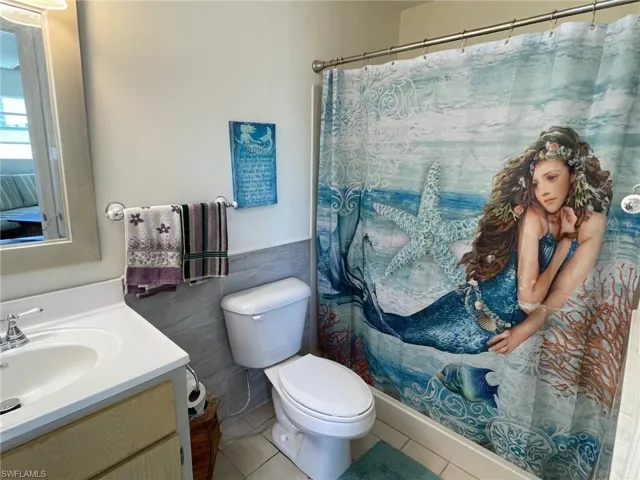 Full bathroom featuring vanity, wainscoting, tile patterned floors, toilet, and tile walls
