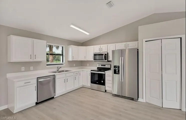 Kitchen with light hardwood / wood-style floors, stainless steel appliances, sink, lofted ceiling, and white cabinetry
