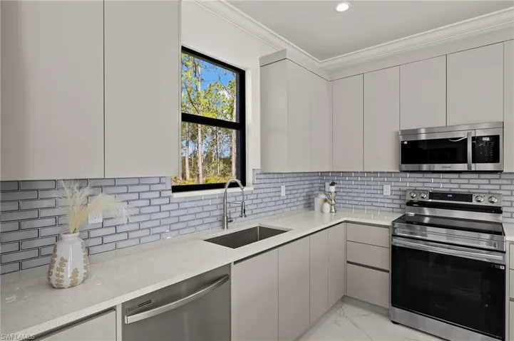 Kitchen featuring crown molding, marble finish floor, modern cabinets, stainless steel appliances, and a sink