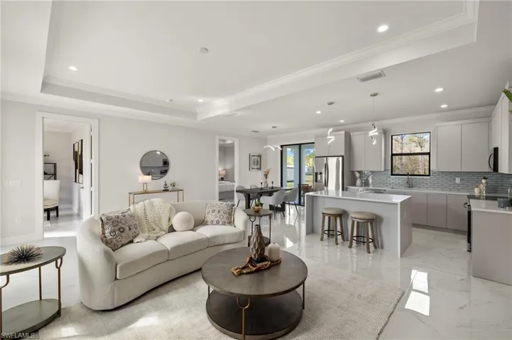 Living room featuring a tray ceiling, recessed lighting, ornamental molding, marble finish floor, and visible vents