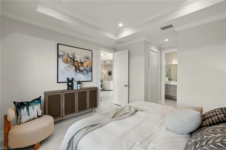 Bedroom with a tray ceiling, crown molding, ensuite bath, marble finish floor, and visible vents