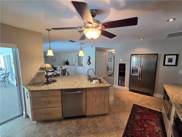 Kitchen with appliances with stainless steel finishes, ceiling fan, light stone counters, and decorative light fixtures