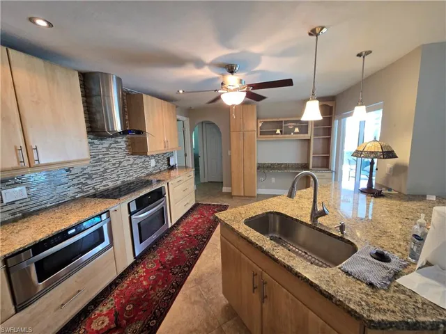 Kitchen with stainless steel oven, wall chimney range hood, black electric stovetop, backsplash, and arched walkways