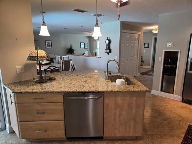 Kitchen featuring stainless steel appliances, pendant lighting, light stone countertops, and brown cabinets