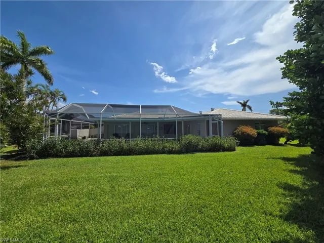 Rear view of property featuring a yard, glass enclosure, and a tiled roof