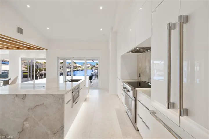 Kitchen with modern cabinets, premium appliances, white cabinetry, light stone counters, and a water view