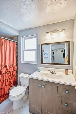 Bathroom featuring toilet, vanity, a shower with shower curtain, a textured wall, and a textured ceiling