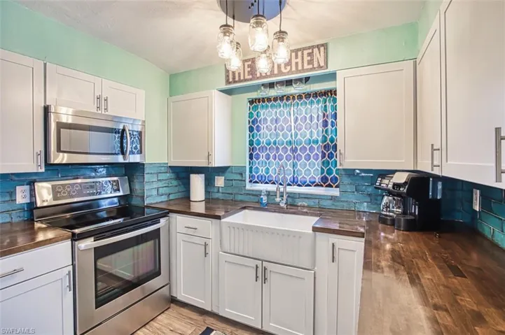 Kitchen with appliances with stainless steel finishes, wooden counters, a sink, backsplash, and light wood-style floors