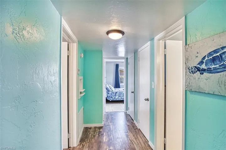Hall with wood finished floors, a textured wall, and baseboards