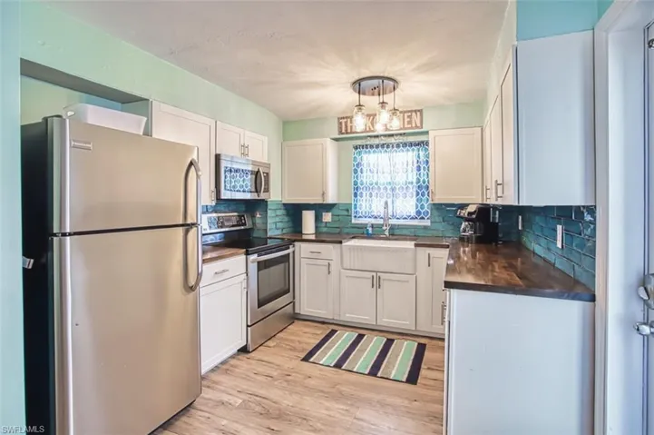 Kitchen with stainless steel appliances, dark countertops, a sink, light wood-style flooring, and backsplash
