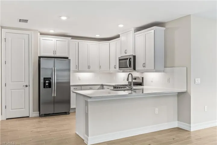 Kitchen featuring stainless steel appliances, wood finish floors, white cabinets, backsplash, and recessed lighting