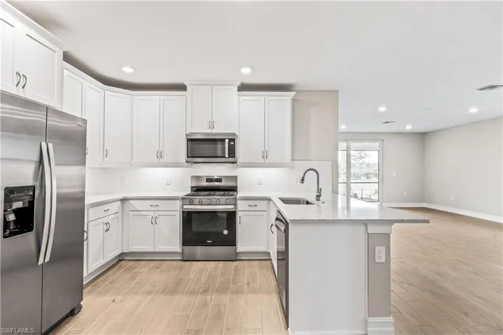 Kitchen featuring stainless steel appliances, a peninsula, white cabinets, light wood-style flooring, and recessed lighting