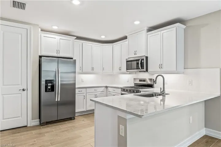 Kitchen featuring appliances with stainless steel finishes, wood finish floors, white cabinets, and recessed lighting
