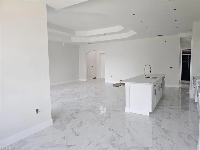 Kitchen featuring light tile flooring, a center island with sink, a raised ceiling, white cabinets, and sink