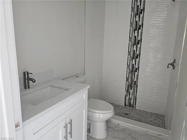 Bathroom with tile flooring, tiled shower, toilet, and vanity