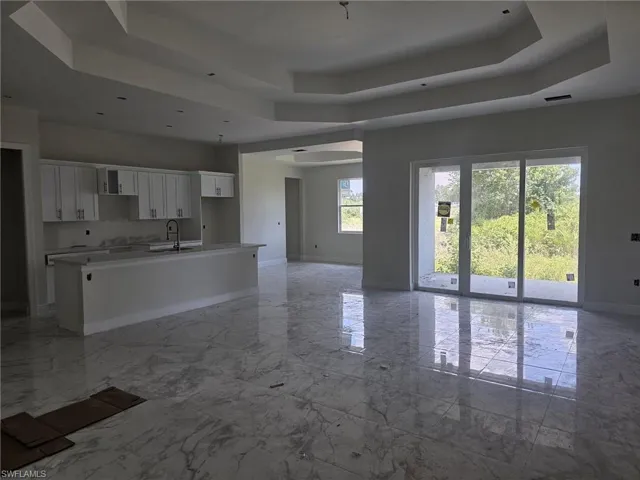 Kitchen featuring an island with sink, white cabinets, sink, light tile floors, and a raised ceiling