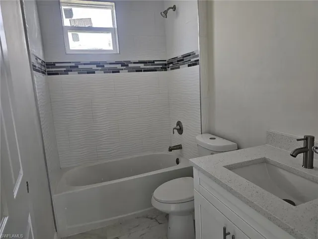 Full bathroom with tile flooring, tiled shower / bath combo, vanity, and toilet