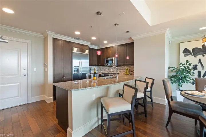 Kitchen featuring light stone counters, stainless steel appliances, ornamental molding, dark wood-style flooring, and dark brown cabinets