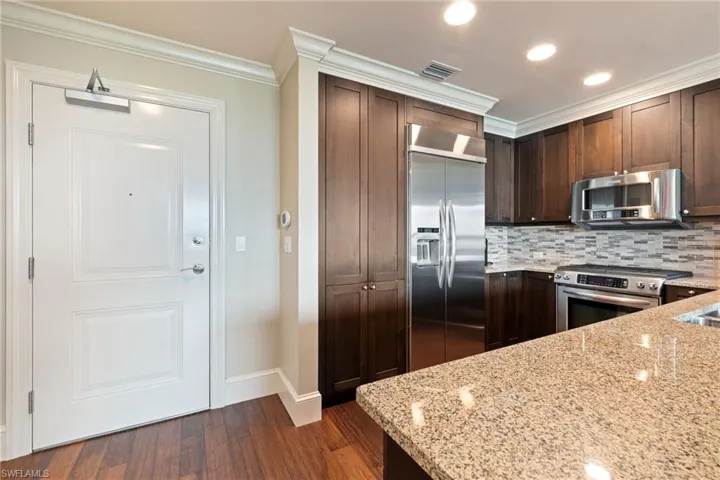 Kitchen with stainless steel appliances, crown molding, light stone counters, dark wood-style floors, and tasteful backsplash