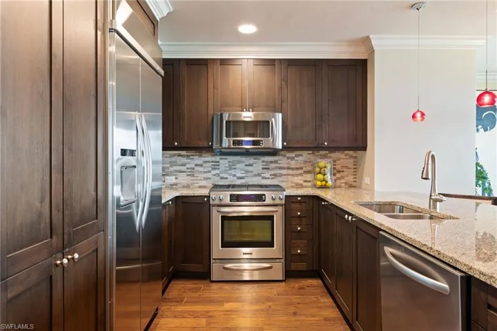 Kitchen featuring stainless steel appliances, wood finished floors, dark brown cabinets, ornamental molding, and backsplash