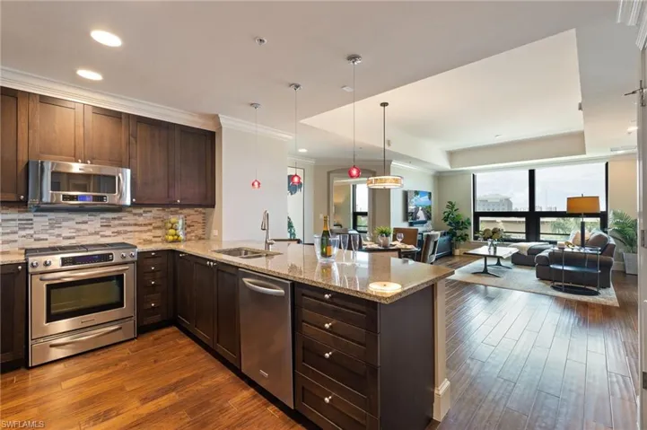 Kitchen featuring appliances with stainless steel finishes, dark wood finished floors, open floor plan, a peninsula, and light stone countertops