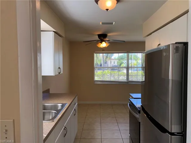 Kitchen with light tile flooring, white cabinets, sink, and stainless steel refrigerator