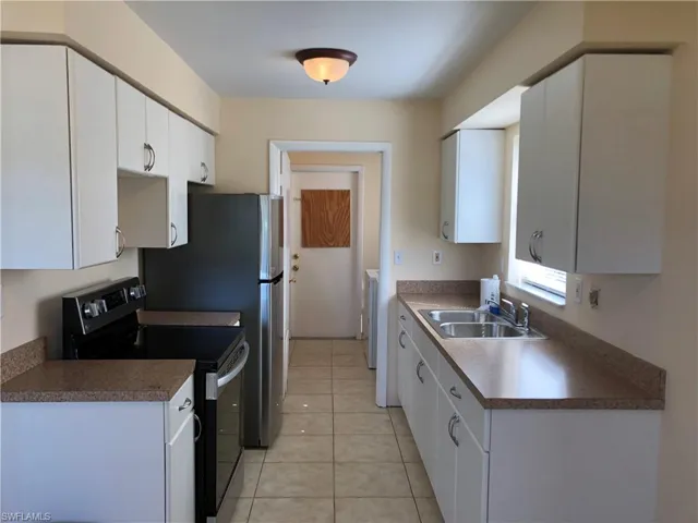 Kitchen with white cabinetry, light tile floors, sink, and electric stove