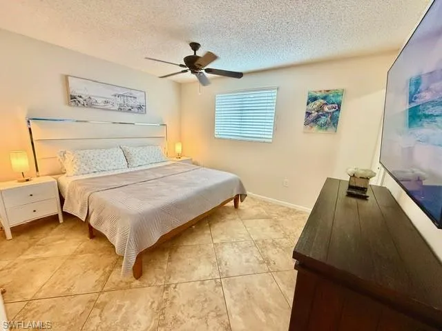 Bedroom with ceiling fan, a textured ceiling, and light tile patterned floors