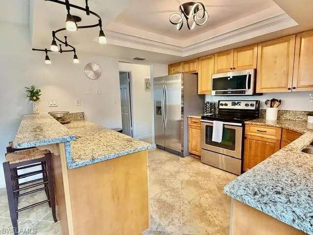 Kitchen with stainless steel appliances, light stone countertops, a breakfast bar area, pendant lighting, and crown molding