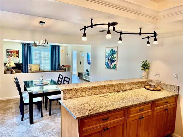 Kitchen with a peninsula, brown cabinets, light stone countertops, decorative light fixtures, and a chandelier