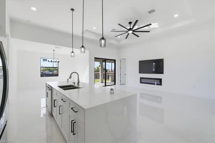 Kitchen with light stone counters, a center island with sink, white cabinetry, ceiling fan, and pendant lighting