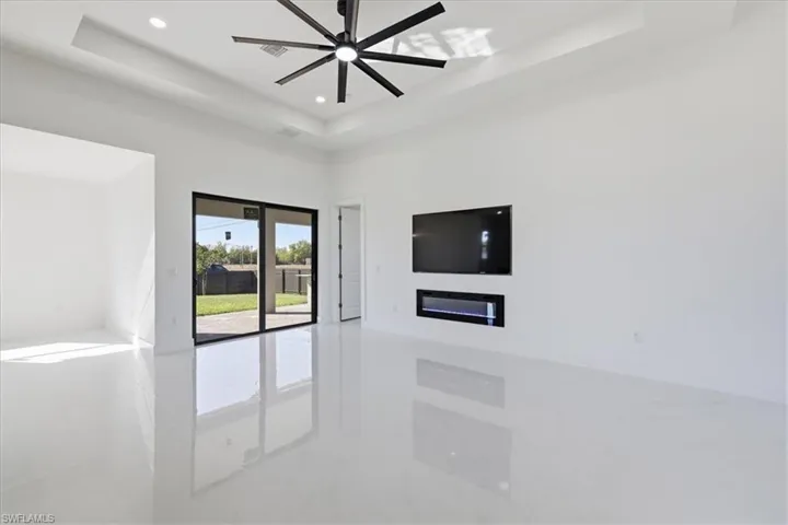 Unfurnished living room featuring recessed lighting, a raised ceiling, ceiling fan, and a glass covered fireplace