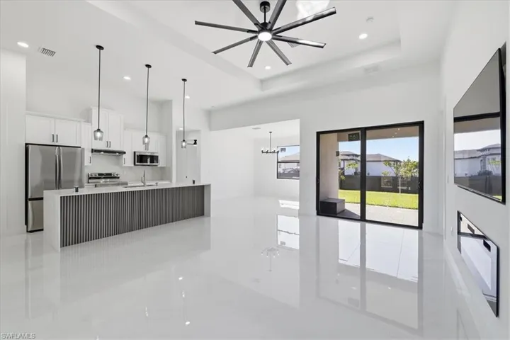 Kitchen featuring white cabinetry, stainless steel appliances, suspended lighting, an island with sink, and light stone countertops