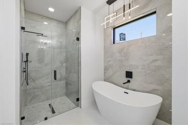 Full bath featuring a marble finish shower, a freestanding bath, tile walls, and recessed lighting
