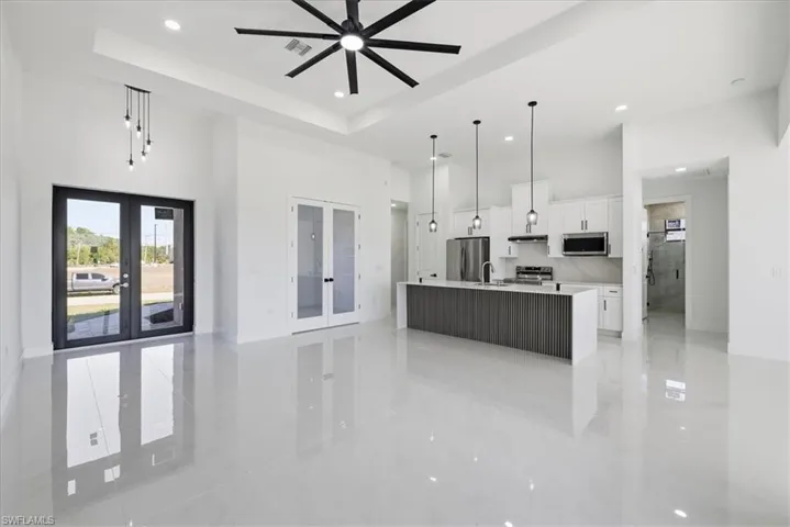 Kitchen featuring a high ceiling, french doors, white cabinets, open floor plan, and a center island with sink