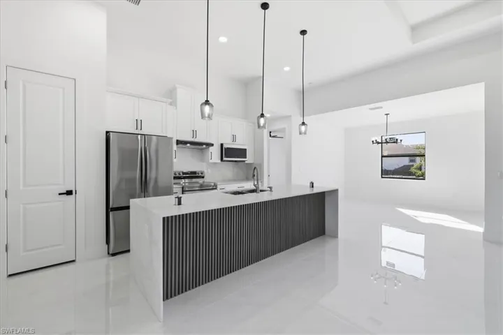 Kitchen with stainless steel appliances, a center island with sink, white cabinetry, and light stone counters