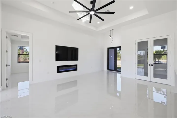 Spare room featuring french doors, a glass covered fireplace, a ceiling fan, recessed lighting, and a raised ceiling