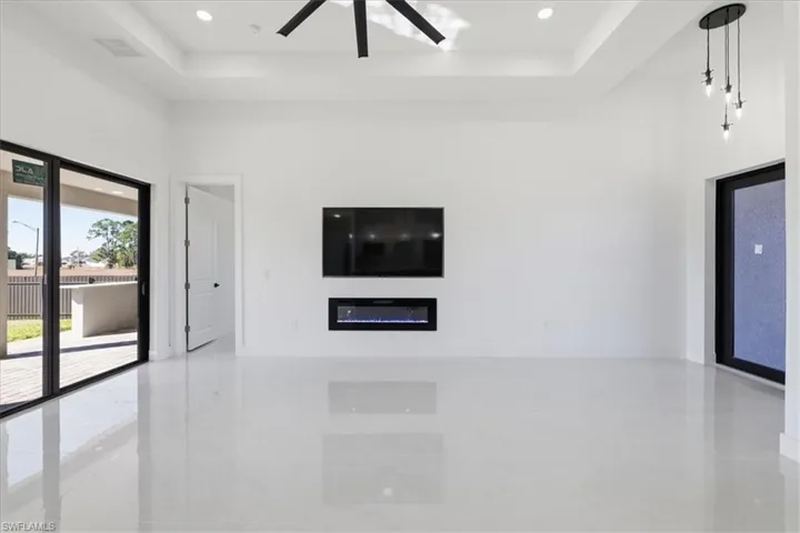Unfurnished living room featuring a tray ceiling, a glass covered fireplace, ceiling fan, and recessed lighting